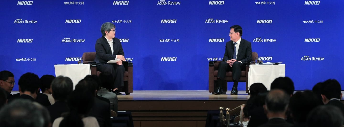 Two people in suits sit on stage with a "Nikkei Asian Review" backdrop, audience facing them.